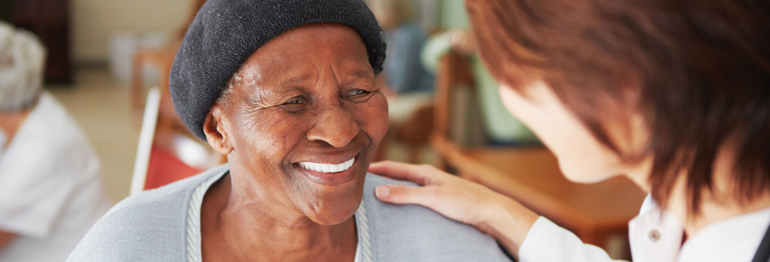 Women smiling at healthcare worker. The healthcare worker has her hand on the woman's shoulder