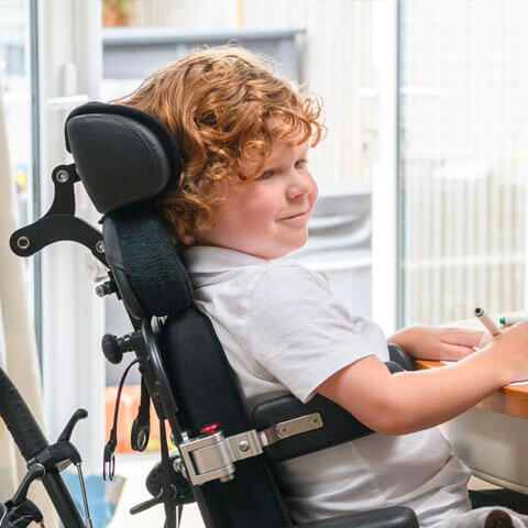 Boy in wheelchair at table while writing